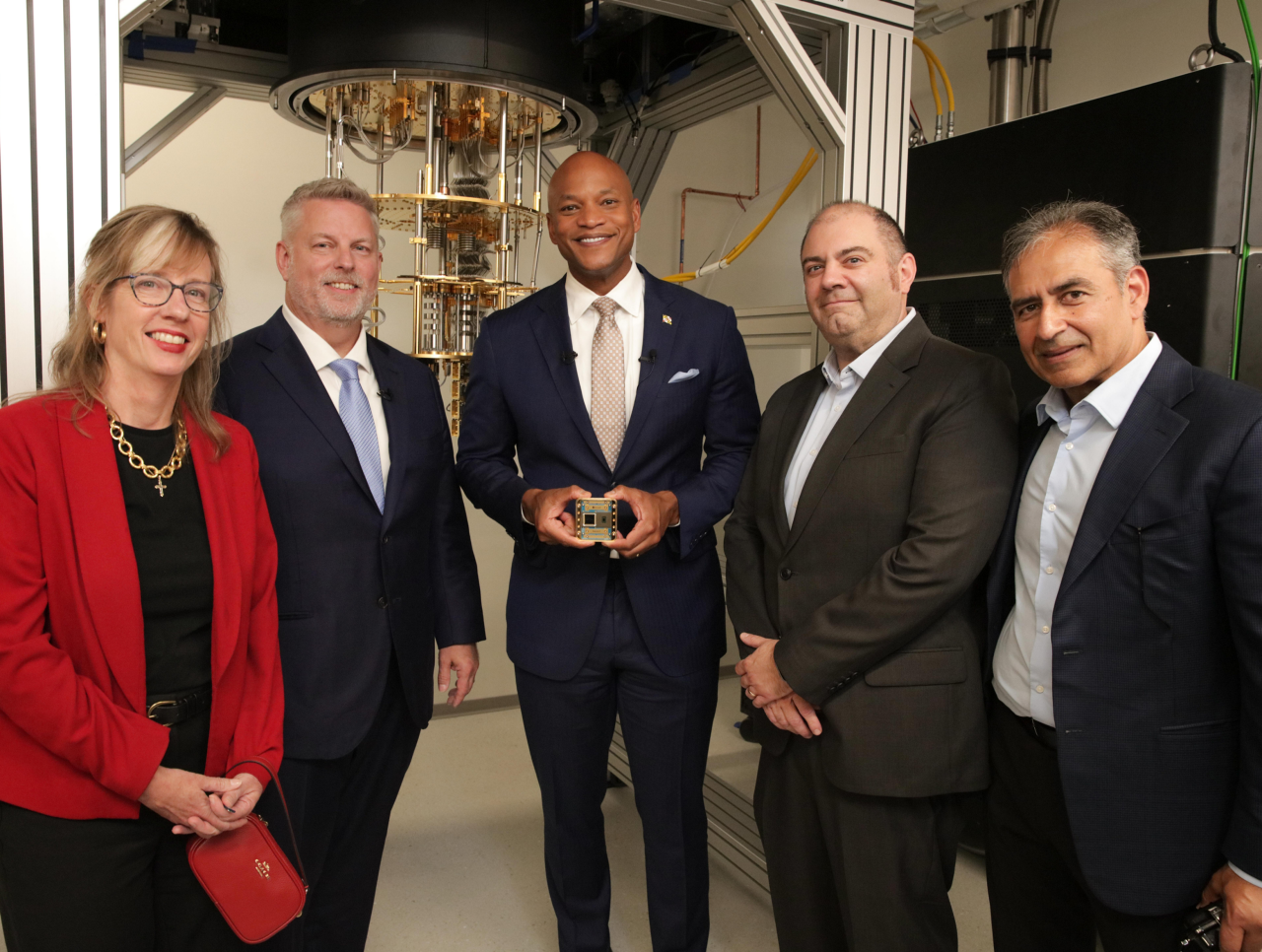 Five people pose beside a quantum computing system in a research laboratory, with one person holding a small device.